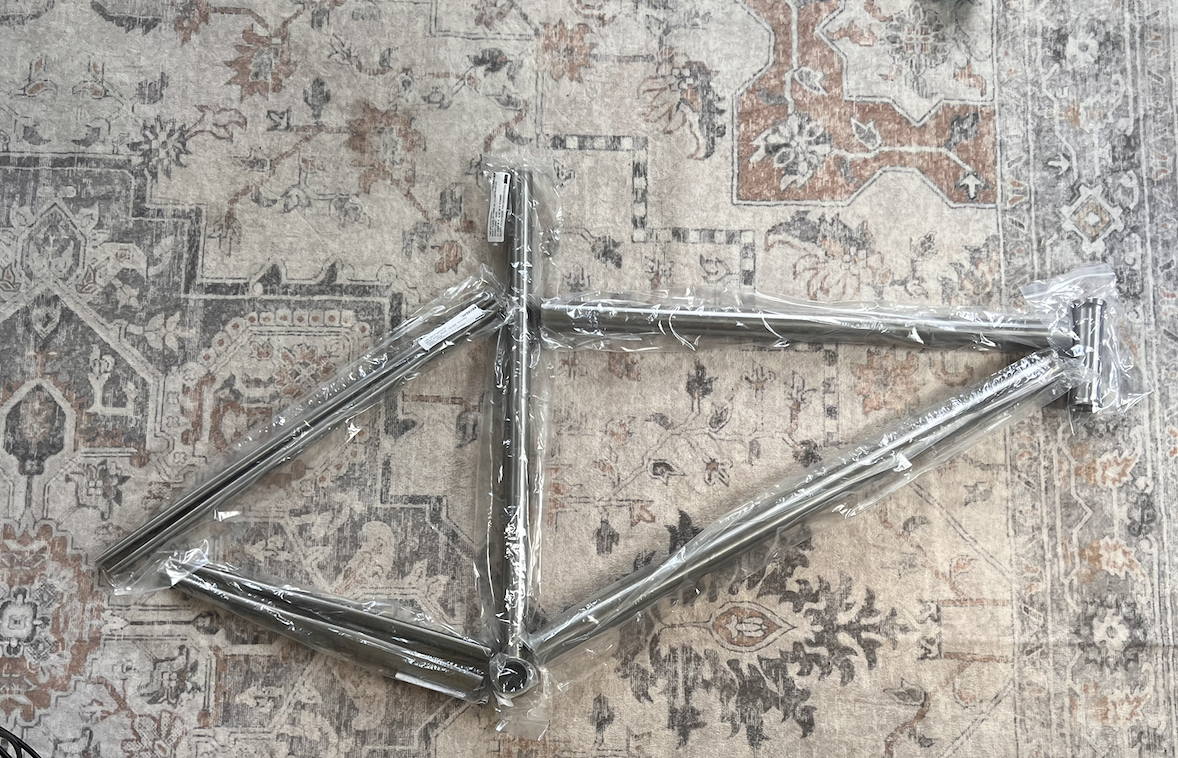 Unwelded road bike frame tubes laid out on a patterned rug.